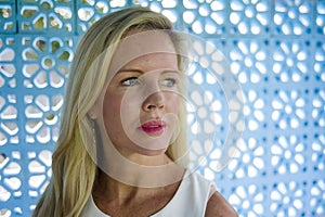 Close up portrait of beautiful and relaxed Caucasian blond woman with blue eyes looking away on a blue pattern background