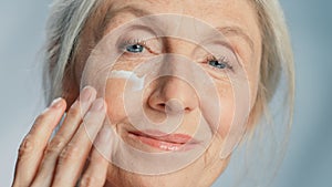 Close-up Portrait of Beautiful Senior Woman Gently Applying Under Eye Face Cream. Elderly Lady Mak