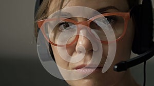 Close-up portrait of beautiful serious woman with headphones and microphone, in glasses reflecting computer screen.