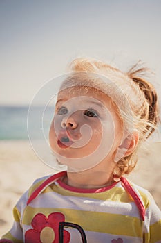 Close up portrait of beautiful small baby, blond little girl in colourful pullover at the beach outdoors.