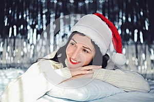 Close up portrait of beautiful smiling brunette young woman with red lipstick, white sweater, Santa Claus hat lying on