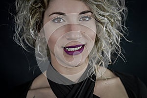 Close up portrait of a beautiful smiling curly blonde woman with purple lipstick and a black top