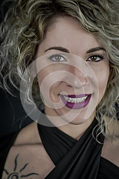 Close up portrait of a beautiful smiling curly blonde woman with purple lipstick and a black top