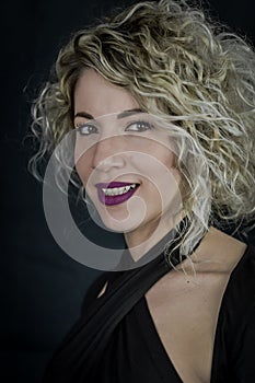 Close up portrait of a beautiful smiling curly blonde woman with purple lipstick and a black top