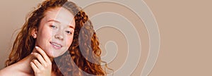 Close-up portrait of a beautiful smiling girl with long curly red hair looks on a beige background. No makeup, no retouching, copy