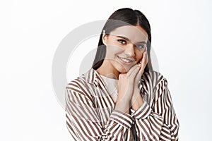 Close up portrait of beautiful smiling woman, gently touching natural clean skin face, gazing at camera delighted