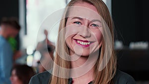 Close-up portrait of beautiful smiling young Caucasian blonde leader business woman posing at camera at trendy office.