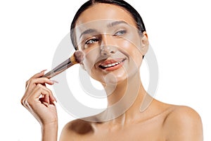 Close up portrait of beautiful woman applying dry cosmetic foundation on face with makeup brush