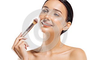 Close up portrait of beautiful woman applying dry cosmetic foundation on face with makeup brush