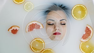 Close-up portrait of beautiful woman face in milk bath filled with fruit,