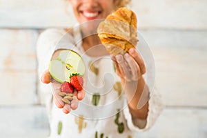 Close up and portrait of beautiful woman showing at the camera healthy food like fruit and in the other hand bad alimentation like