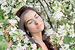 Close-up portrait of a beautiful woman in a spring garden. A girl with her eyes closed inhales the fragrance of flowering trees