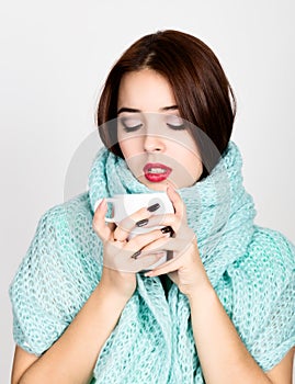 Close-up portrait of a beautiful woman in woolen scarf, drinking hot tea or coffee from white cup