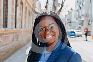 Close up portrait of a beautiful young african american woman with pigtail hairstyle in a blue jacket and glasses smiling and