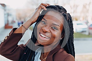 Close up portrait of a beautiful young african american woman with pigtails hairstyle in a brown business suit walks along spring