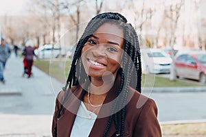 Close up portrait of a beautiful young african american woman with pigtails hairstyle in a brown business suit walks along spring