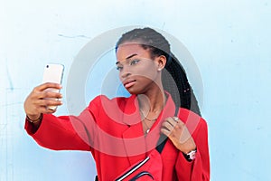 Close up portrait of a beautiful young african american woman with pigtails hairstyle in red business suit taking selfie using