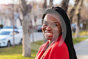 Close up portrait of a beautiful young african american woman with pigtails in a red business suit smiling and walking along the