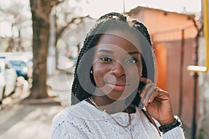 Close up portrait of a beautiful young African American woman with pigtails in a white sweater and beige trousers walks along the