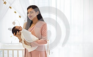 Close up portrait of beautiful young asian mother looking at newborn baby in baby crib room.