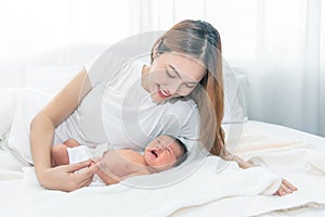 Close up portrait of beautiful young asian mother with newborn baby. Side view of a young woman playing with her little baby in