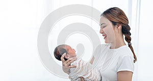 Close up portrait of beautiful young asian mother with newborn baby. Side view of a young woman playing with her little baby