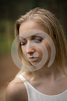 Close up portrait - Beautiful young blonde woman forest nymph in white dress in evergreen wood