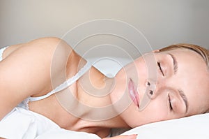 Close up portrait of beautiful young blonde woman sleeping in a white bed