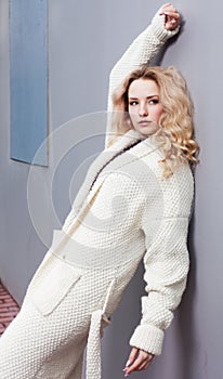 Close up Portrait of a beautiful young blonde woman in a white coat large knitted fashion and sneakers. Streetstyle