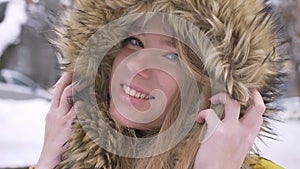 Close-up portrait of beautiful young caucasian girl in fur hood flirtingly posing into camera on winter street
