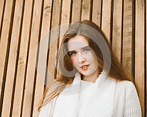 Close up portrait of beautiful young girl with long brown hair on wooden background of planks, winter or autumn outdoor photoshoot