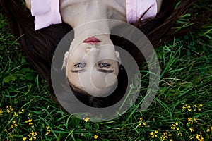 Close up portrait of a beautiful young girl lying on green grass