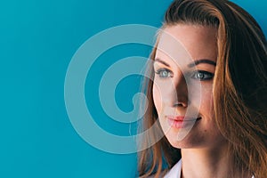 Close-up portrait of beautiful young happy woman on blue background, with space for slogan or text. Nice makeup on face.