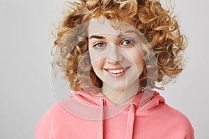 Close-up portrait of beautiful young woman with curls smiling friendly, looking confident and relaxed while taking