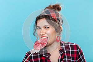 Close up portrait of beautiful young woman eating lollipop over blue background