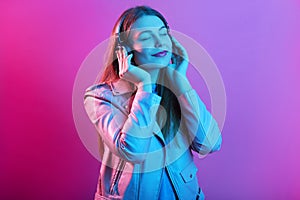 Close up portrait of beautiful young woman in headphones listening to music. Happy smiling girl wearing leather pink jacket
