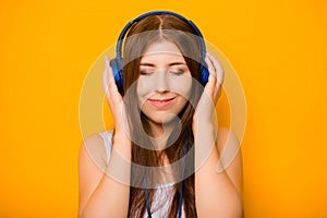 Close Up portrait of a beautiful, young woman listening to music with headphones, standing on a yellow background.