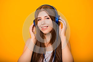 Close Up portrait of a beautiful, young woman listening to music with headphones, standing on a yellow background.