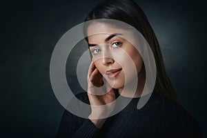 Close-up portrait of beautiful young woman standing at isolated dark background