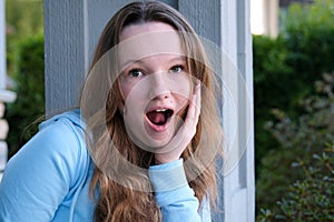 Close up portrait of a beautiful young woman with surprised expression looking at camera. Unbelieving, outdoor.