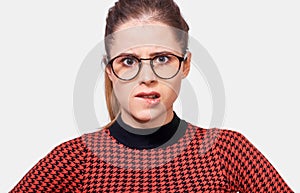 Close-up portrait of beautiful young woman wearing red t-shirt and eyeglasses bits the lips, looking at the camera, uncertain