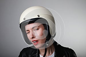 Close-up portrait of biker young woman, making funny face, wearing white helmet, with red lips. Studio background.