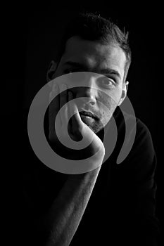 Close up portrait in black and white of a young man holding his face in his hand and looking bored