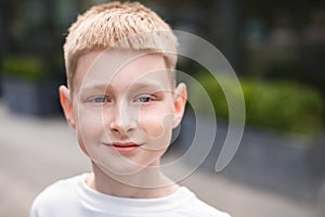 close up portrait of blond boy with blue eyes looking at camera and walking outdoors in city street