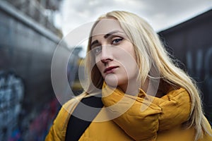 Close up portrait of blonde hipster teen girl making selfie, She is wearing yellow jacket and backpack, walking outdoors throught