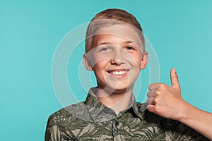 Close-up portrait of a blonde teenage boy in a green shirt with palm print posing against a blue studio background
