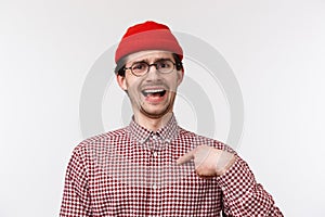 Close-up portrait boastful funny bearded young man in red beanie and glasses, pointing at himself as talking own