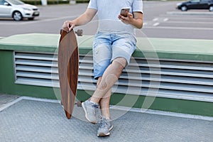 Close up portrait of boy surfing in web using a cellphone, near the longboard, chatting in social networks
