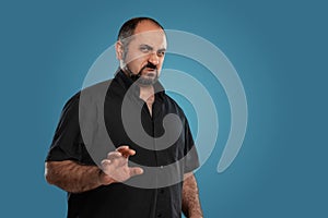 Close-up portrait of a brunet middle-aged man with beard, dressed in a black t-shirt and posing against a blue