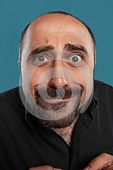 Close-up portrait of a brunet middle-aged man with beard, dressed in a black t-shirt and posing against a blue